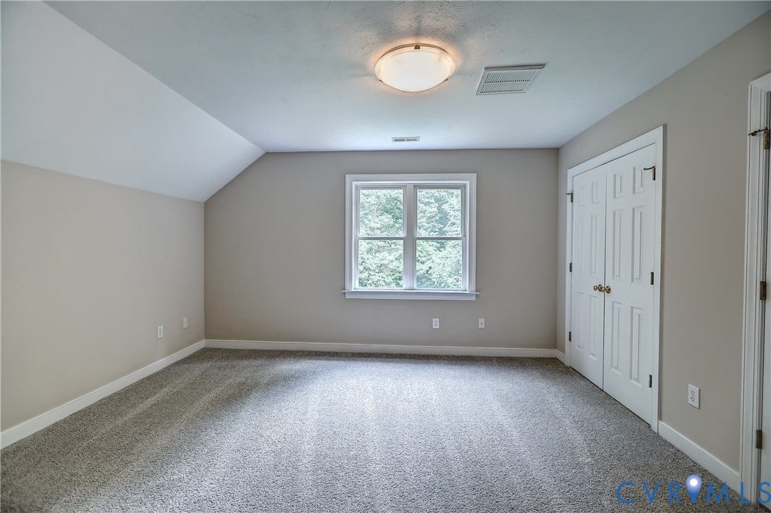 Wall-to-wall carpeting with a neutral color palette, a rectangular window with white trim, a flush mount ceiling light fixture, and bifold closet doors