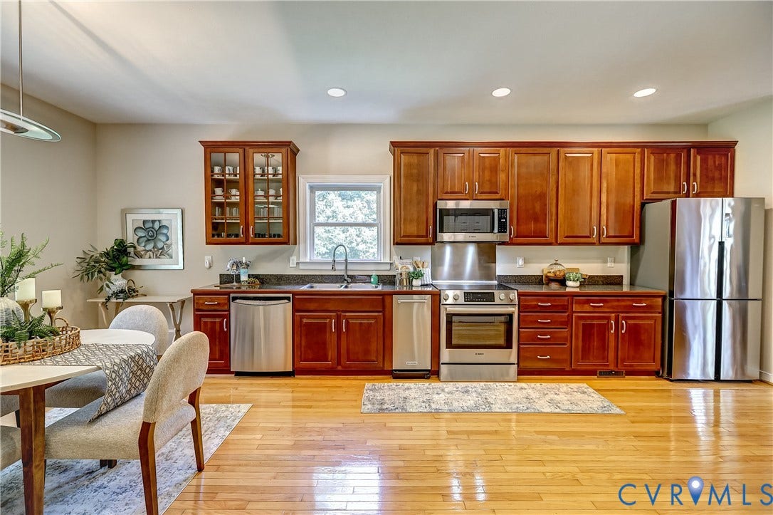 Open-concept kitchen featuring wood-finish flooring, full suite of stainless steel appliances, dark countertops, and ample wood cabinetry