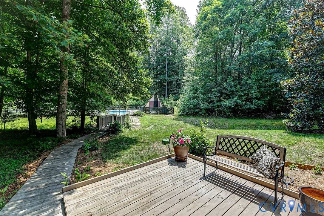 Expansive outdoor deck with a wooden walkway leading to a private pool area, surrounded by mature trees and lush greenery