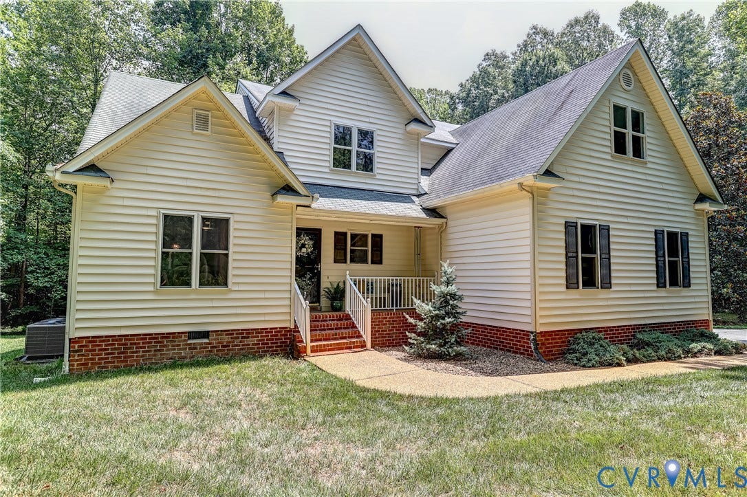 Cream siding exterior with black shutters, a covered porch, and a red brick foundation