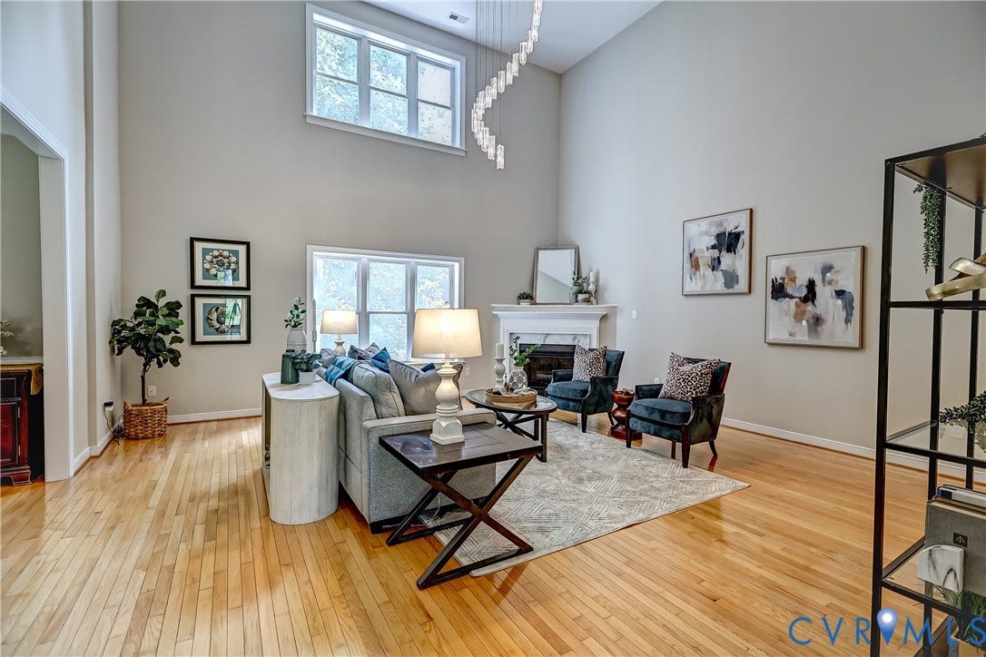 Vaulted ceiling living room featuring wood-finish flooring, a fireplace with a white mantel, and multiple windows
