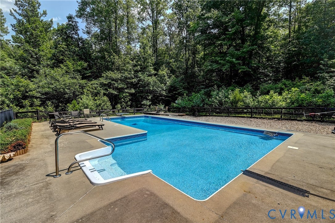 In-ground swimming pool with integrated steps, surrounded by a concrete pool deck and mature trees