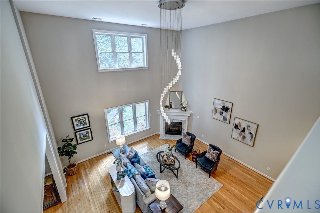 Vaulted ceiling, hardwood flooring, fireplace, white mantel, and a spiral chandelier