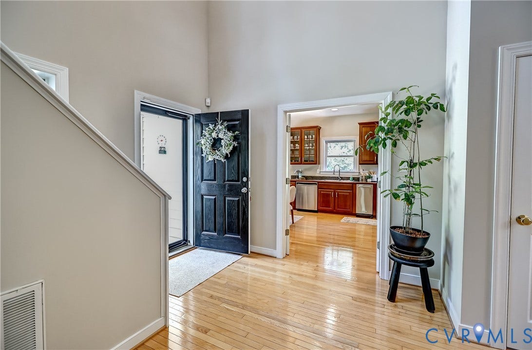 Wood-finish flooring throughout, with a paneled entry door and a clear sightline into the kitchen featuring wood cabinetry and stainless steel appliances