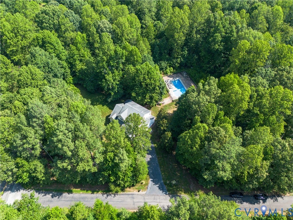 Property with an in-ground swimming pool, surrounded by mature trees, and an asphalt driveway