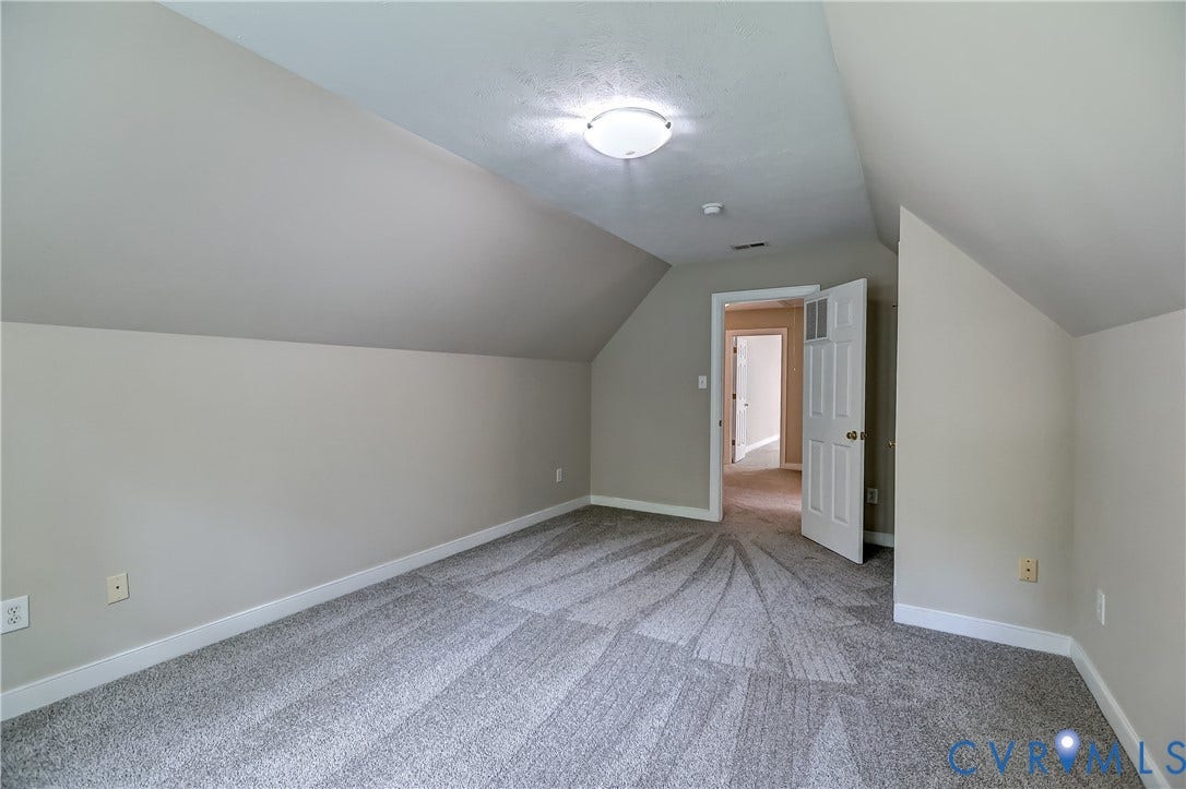 Carpeted flooring, vaulted ceiling, white trim, flat panel door, and flush-mount ceiling light