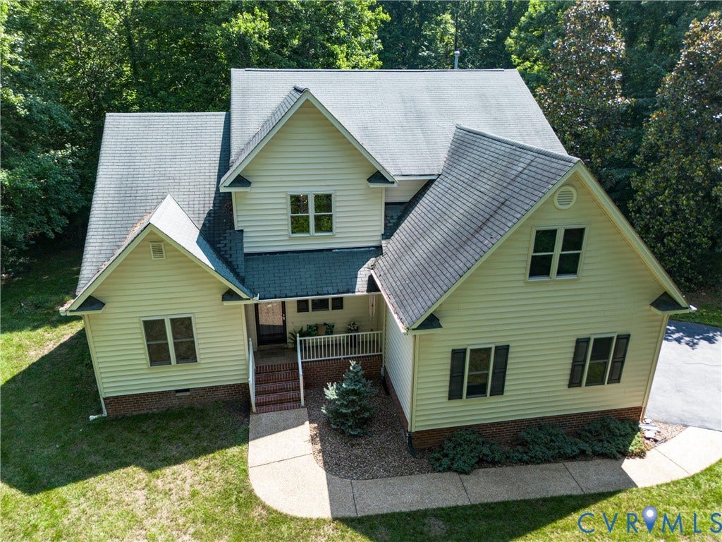Cream-colored siding exterior with dark shutters, multiple gables, covered porch, and mature landscaping