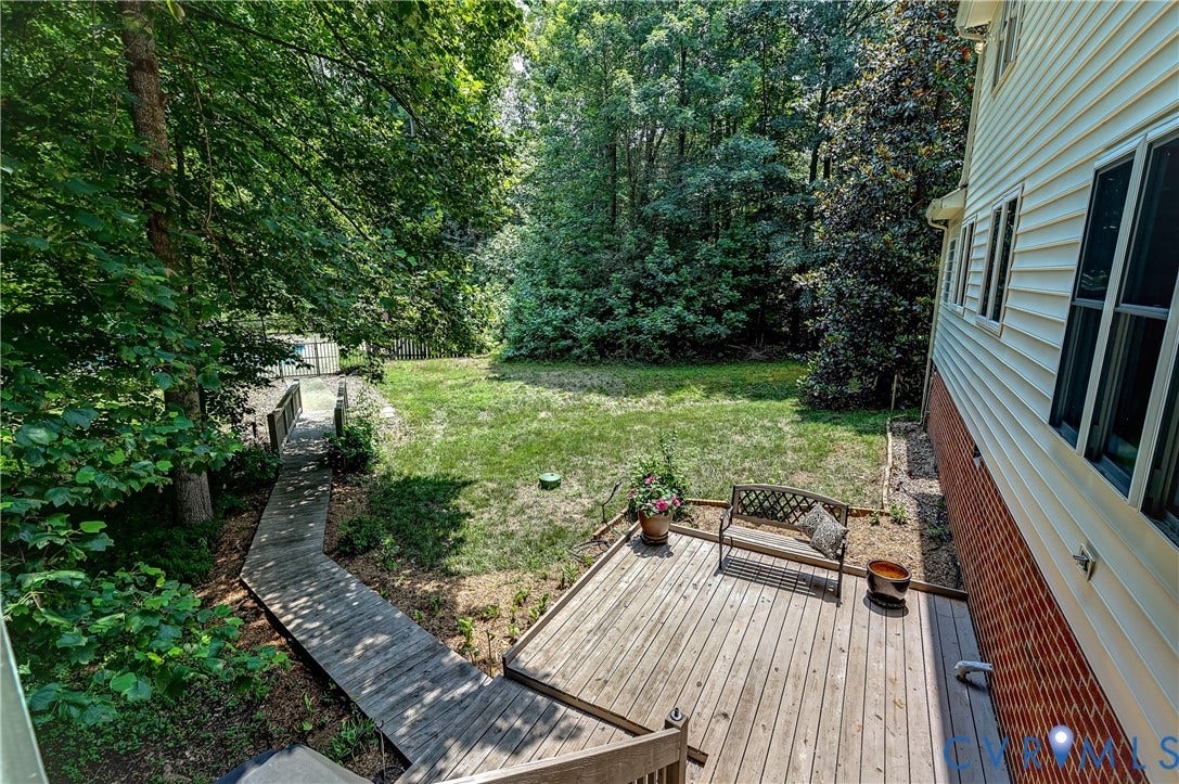 Expansive backyard featuring a manicured lawn, mature trees, a wooden deck, and a wooden walkway