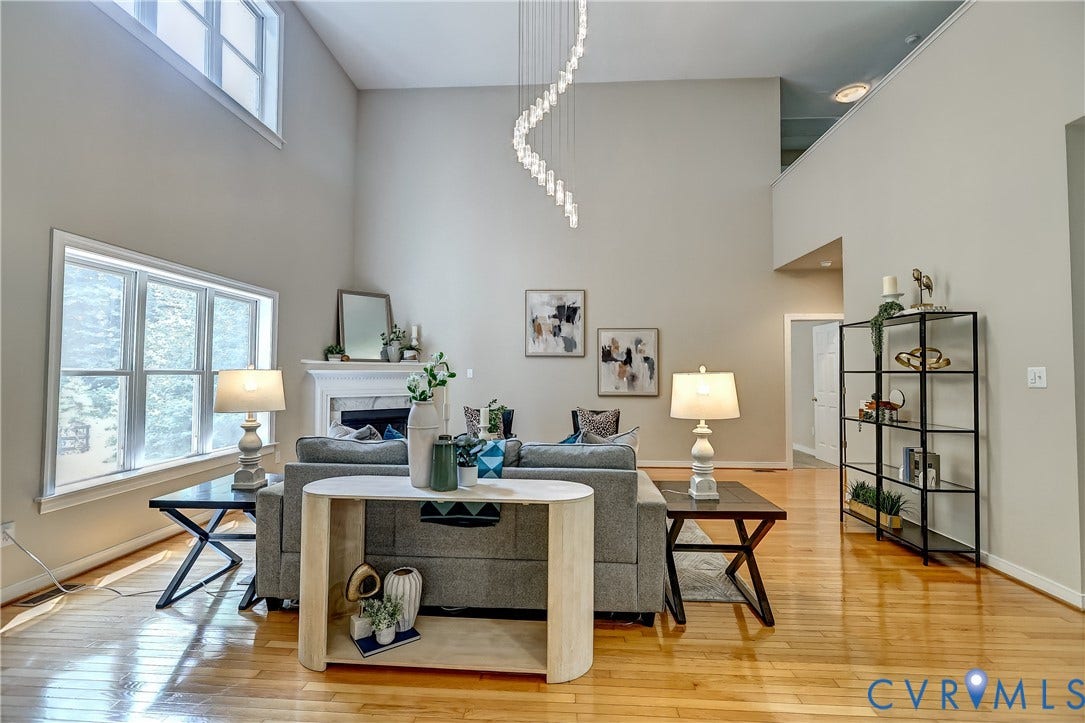 Vaulted ceiling with an elongated pendant light fixture, wood-finish flooring, fireplace with a stone mantel, and large windows