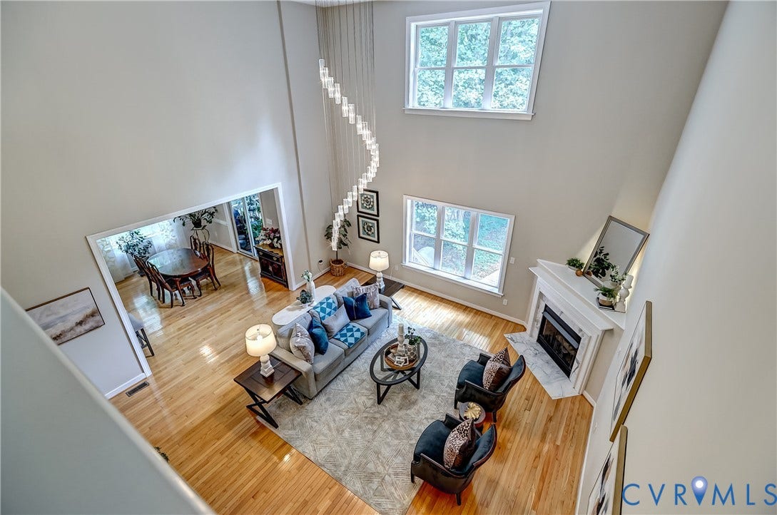 Soaring ceilings with a decorative chandelier, hardwood flooring, fireplace with a mantel, and abundant natural light