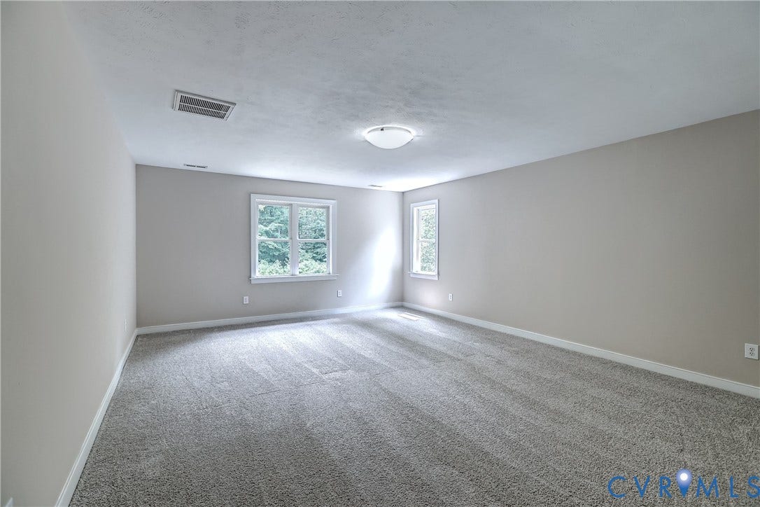 Spacious room featuring neutral-toned walls, gray carpeting, and multiple windows