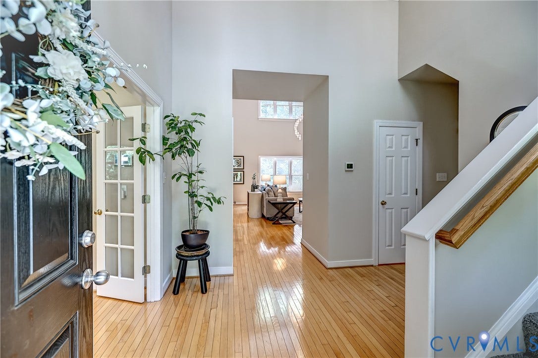 Light wood-finish flooring, a two-story foyer, a solid panel door, and a French door with multiple lites