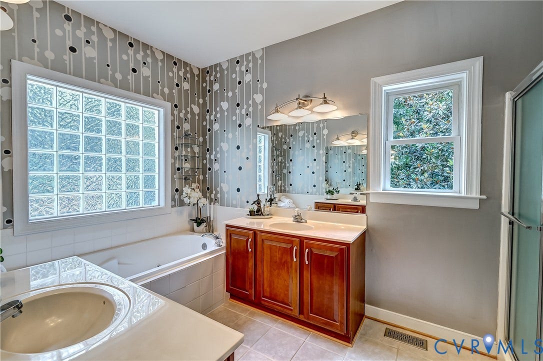 Soaking tub with a glass block window, double vanity with wood cabinetry, and a walk-in shower with a glass enclosure