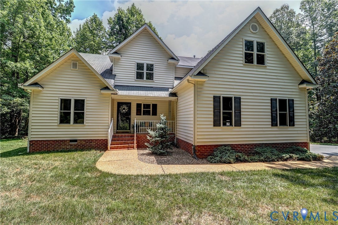 Light-colored siding exterior with dark shutters, multiple gables, a covered front porch, and red brick foundation