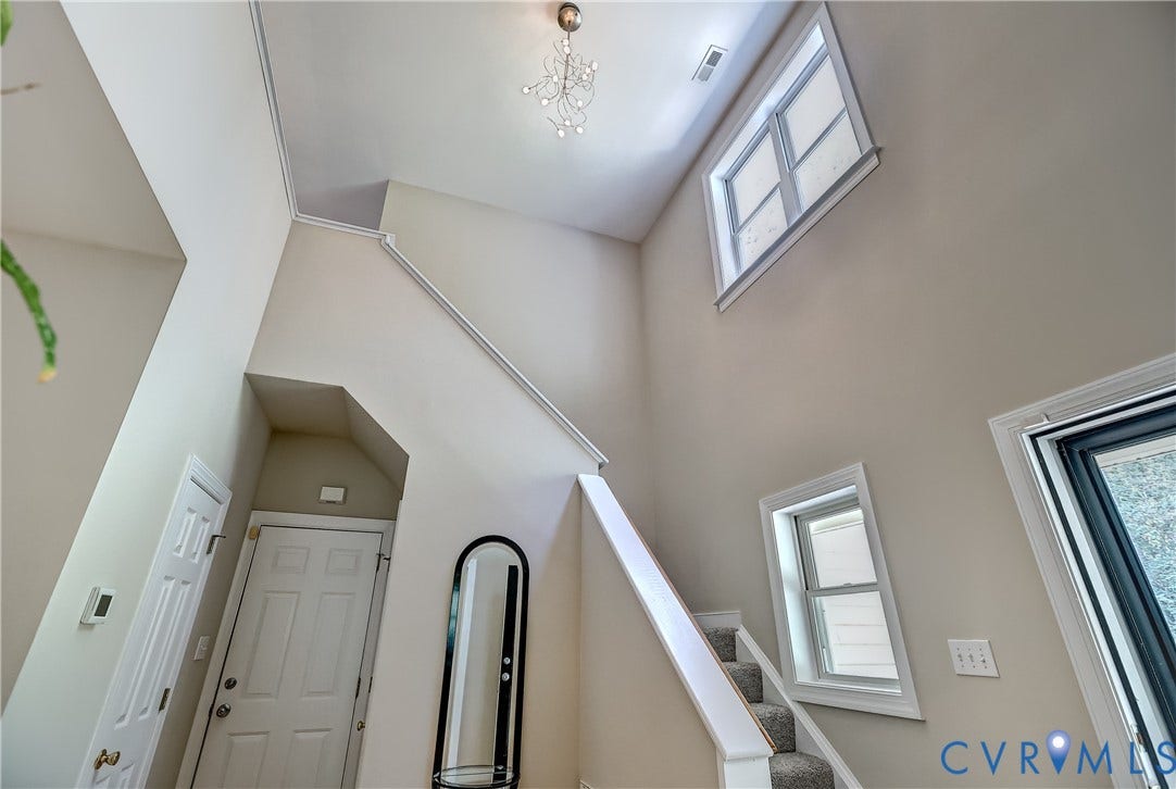 Vaulted ceiling with a chandelier, multiple windows, carpeted staircase, and crown molding