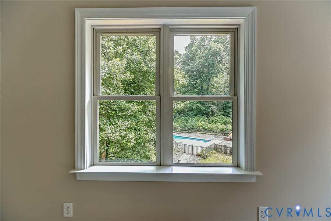Double-hung window with white trim and a white sill overlooking a swimming pool and lush trees