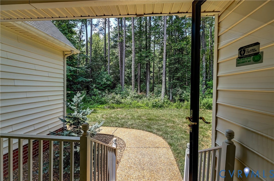 Curved aggregate pathway bordered by landscaping, leading to an expansive natural backyard with mature trees
