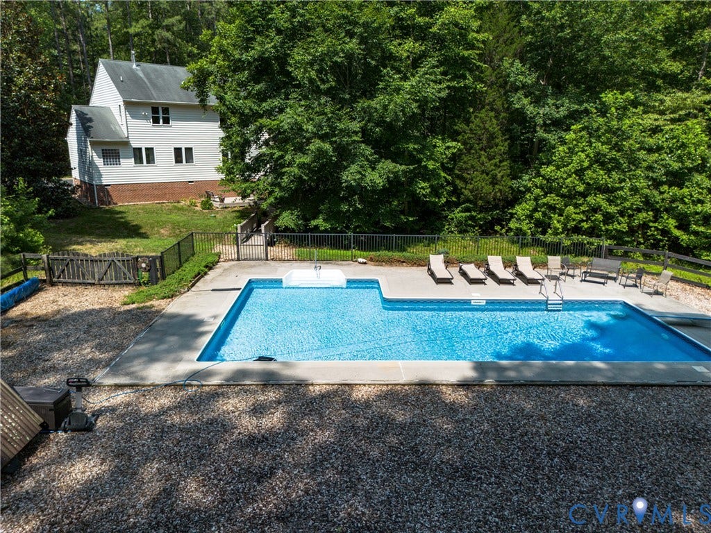 In-ground swimming pool with surrounding concrete decking, black metal fence enclosure, and mature perimeter trees