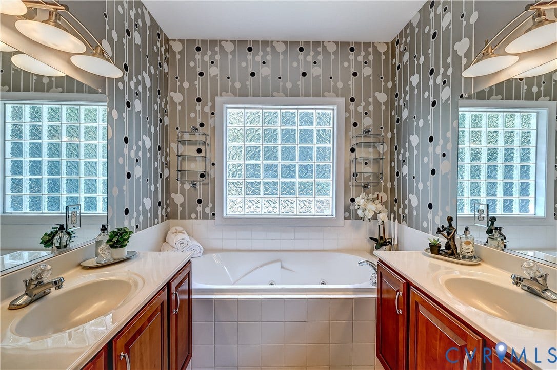 Dual vanity with integrated sinks, recessed soaking tub, glass block windows, and wall-mounted light fixtures