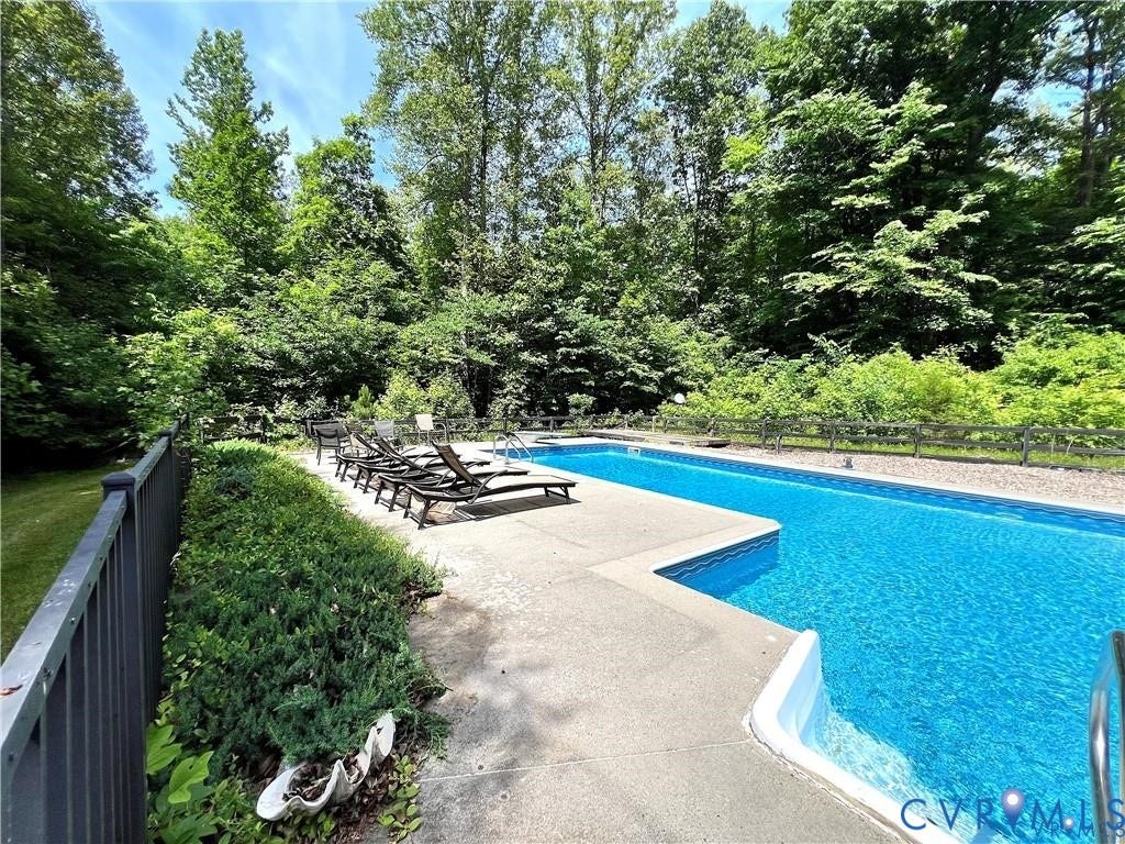 Long rectangular in-ground swimming pool with an integrated spa, concrete decking, and surrounding mature trees