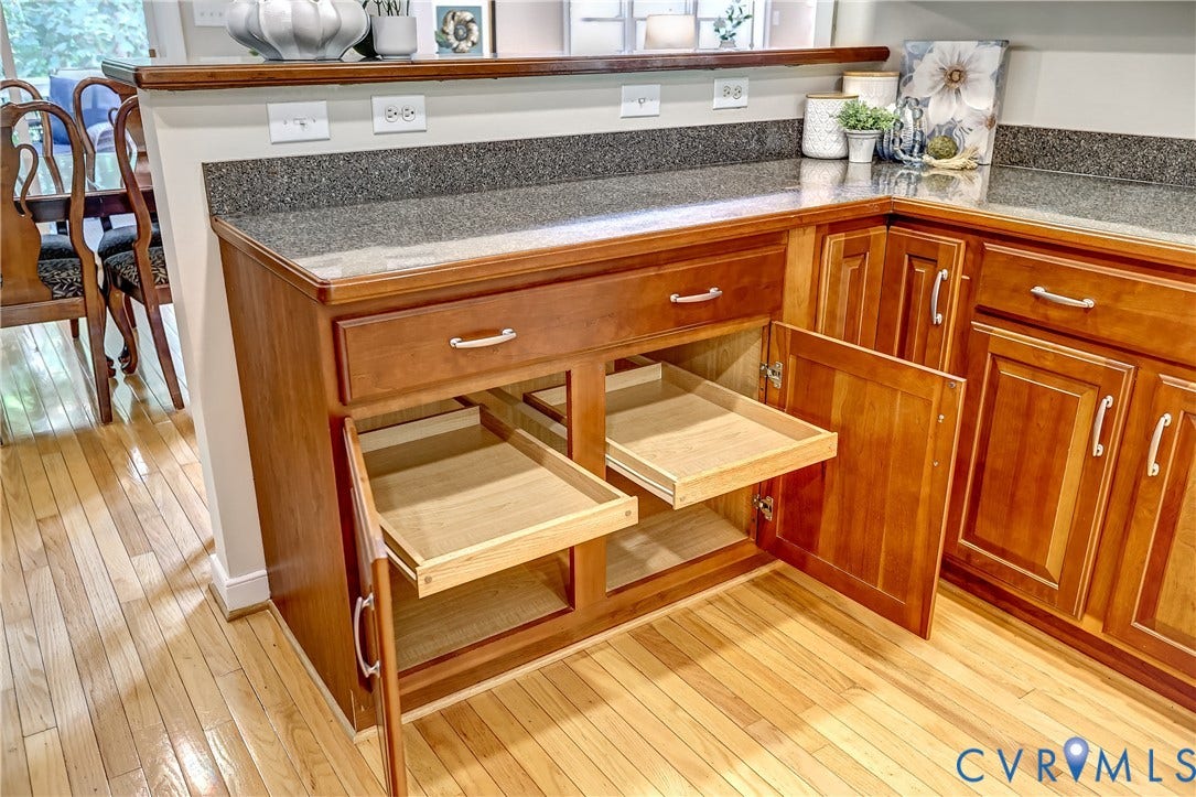 Wood-finish cabinetry with pull-out shelving, stone-finish countertops, and wood-finish flooring
