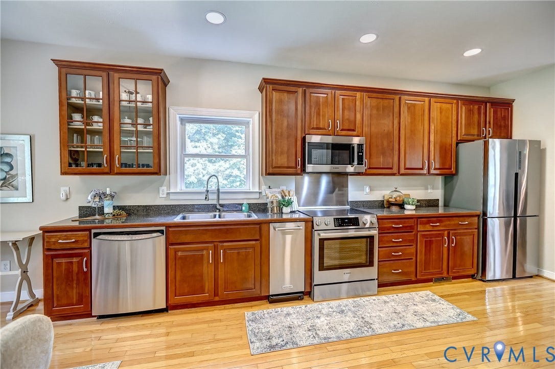 Wood-finish flooring, stainless steel appliances, dark stone countertops, wood cabinetry, and recessed lighting