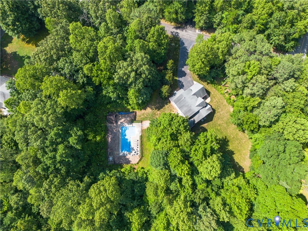 Residential property with a multi-level roofline, surrounded by dense mature trees, featuring a private swimming pool with a paved surround, and an asphalt driveway
