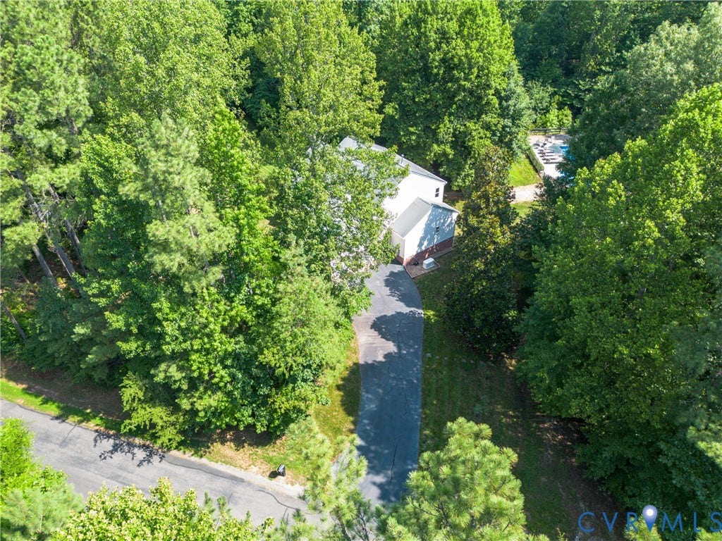 Wooded property featuring a paved driveway, a white-sided residence, and a ground-level swimming pool with a surrounding deck