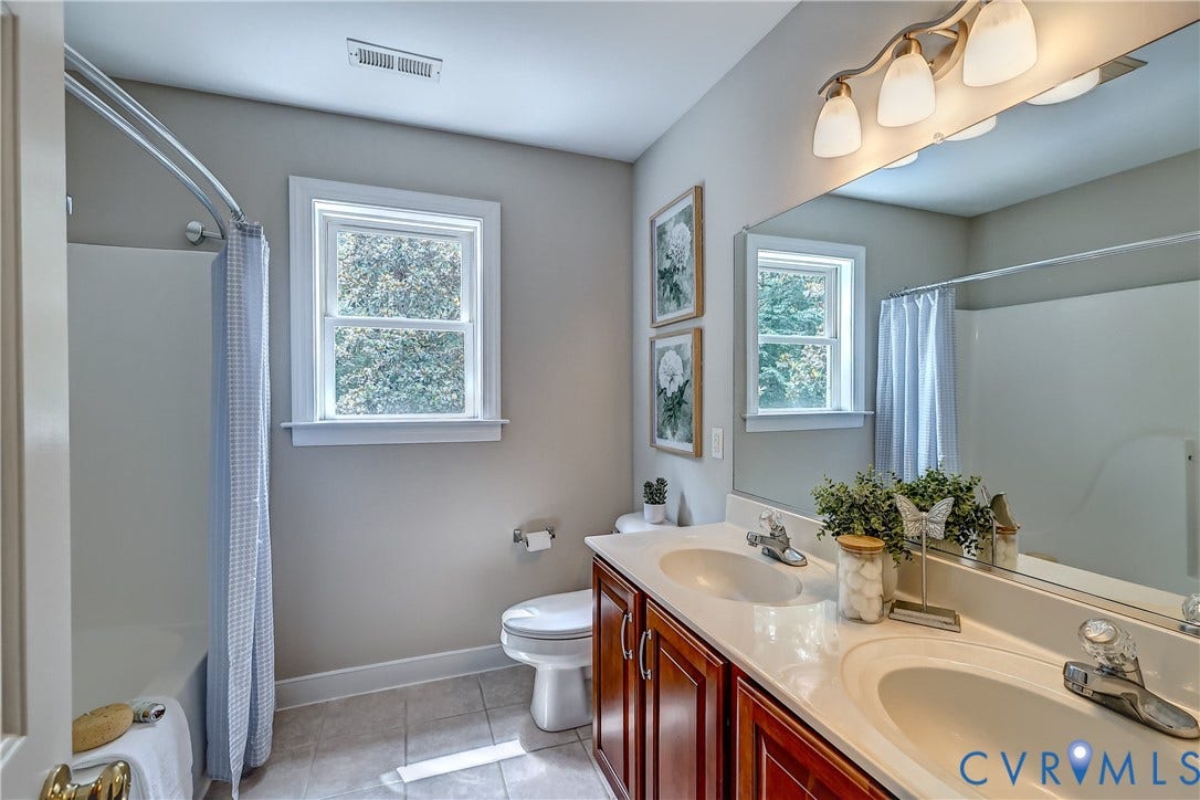 Dual vanity with integrated sinks, wood-finish cabinetry, a large wall-mounted mirror, a bath and shower combination, and a window