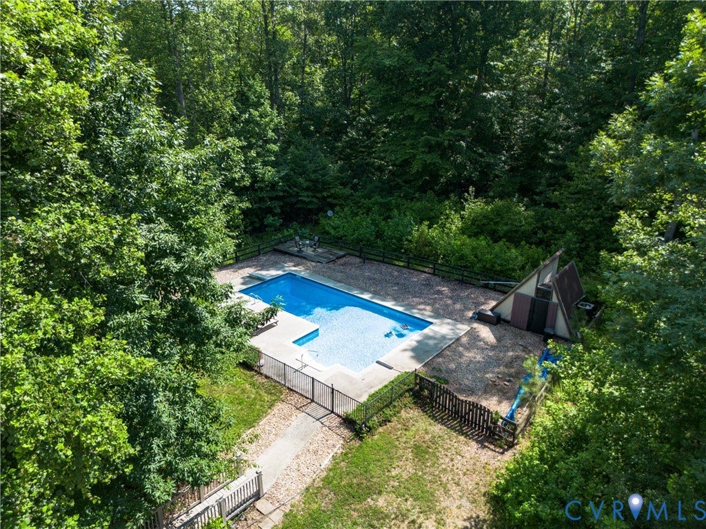 Outdoor swimming pool with concrete surround, A-frame structure, and black fencing, bordered by mature trees