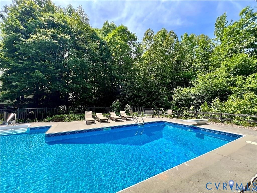 Expansive outdoor pool with integrated steps, surrounded by mature trees and a protective fence