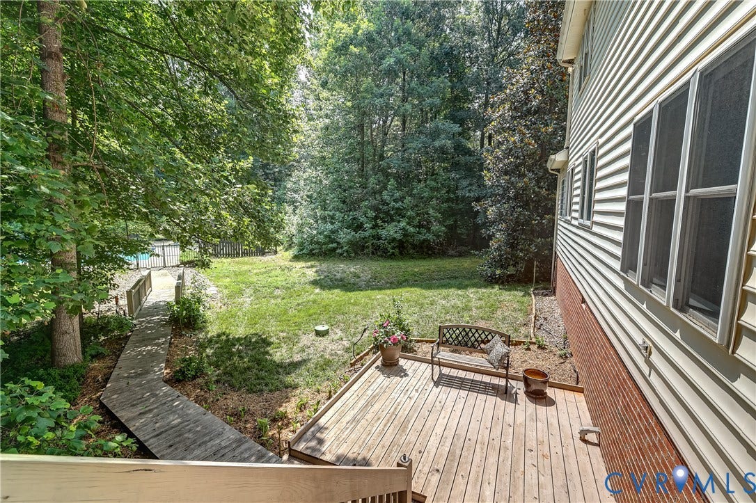 Expansive backyard featuring a wood deck, wood pathway, and mature trees