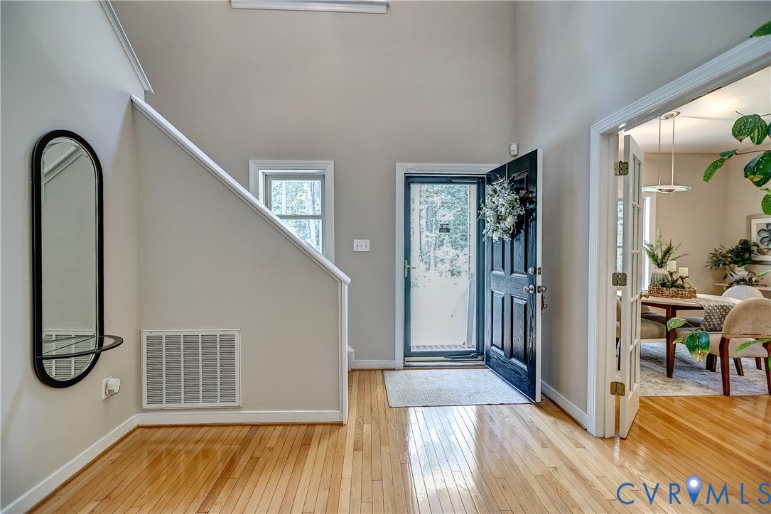 Hardwood flooring throughout the entry, a dark paneled front door, a light-filled transom window, and white trim