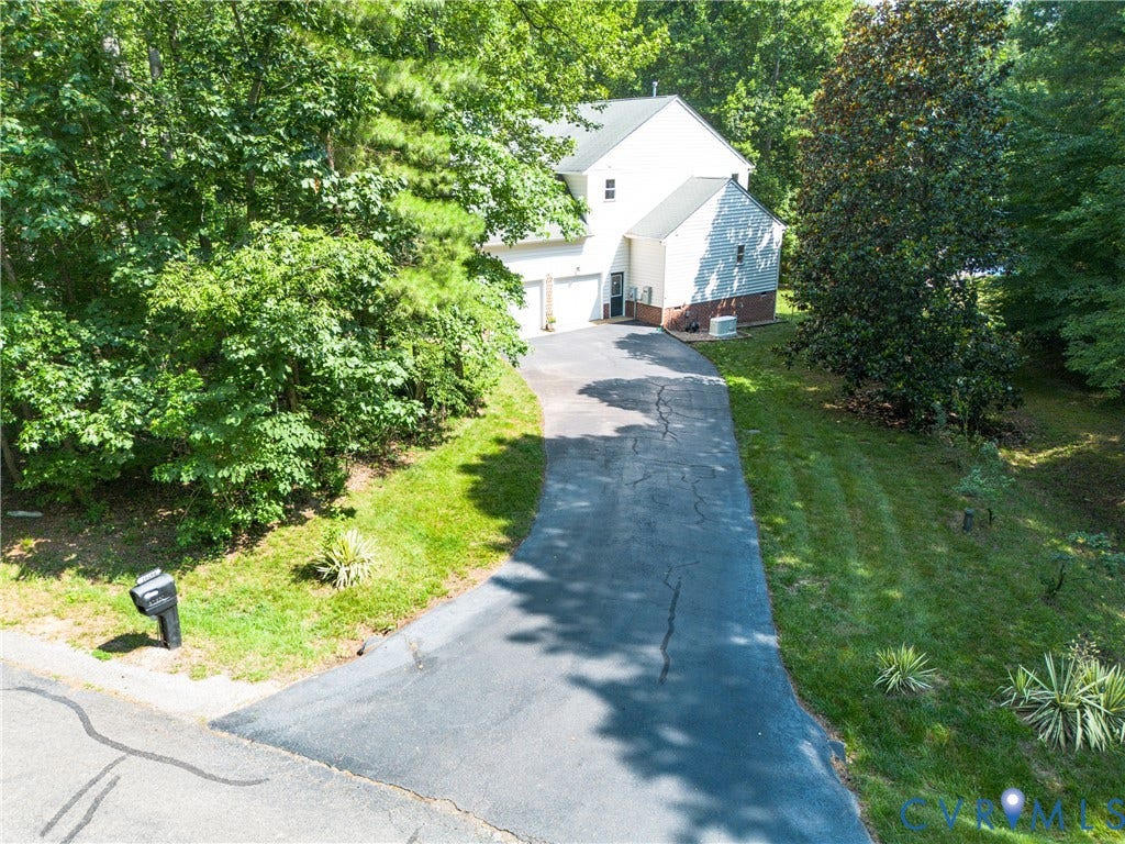 Two-story residence with a two-car garage, long asphalt driveway, and mature trees