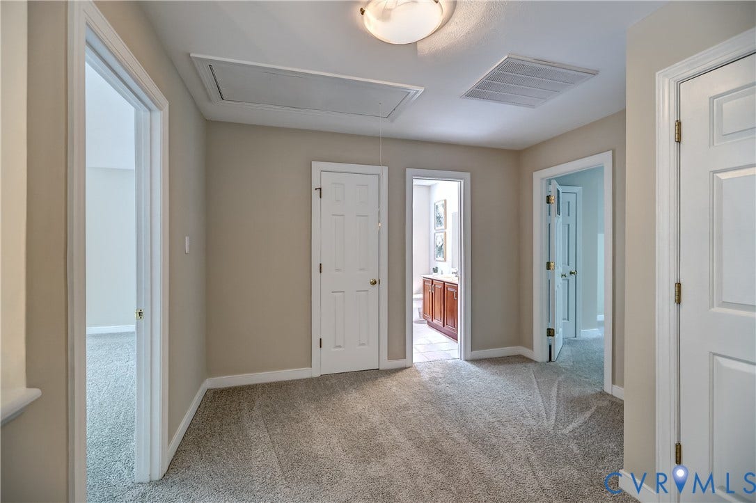 Neutral tone wall paint, carpeted flooring, multiple doorways, a ceiling-mounted light fixture, and an attic access panel