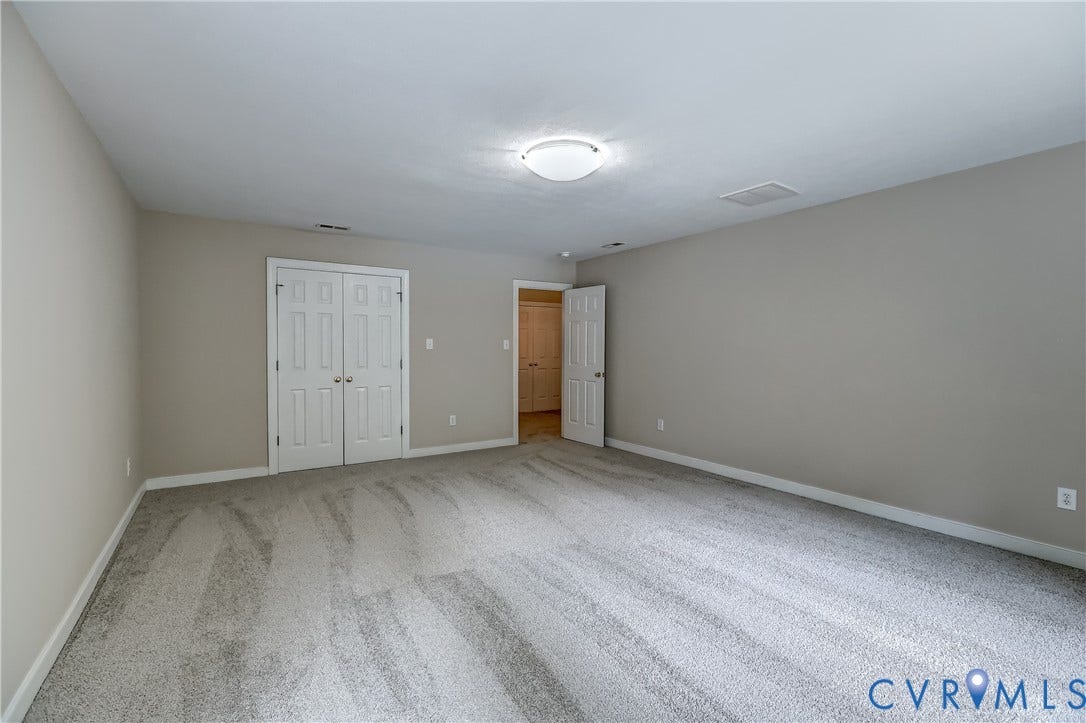 Expansive room with neutral carpeting, light gray wall paint, a white flush-mount ceiling light, and white double-panel doors