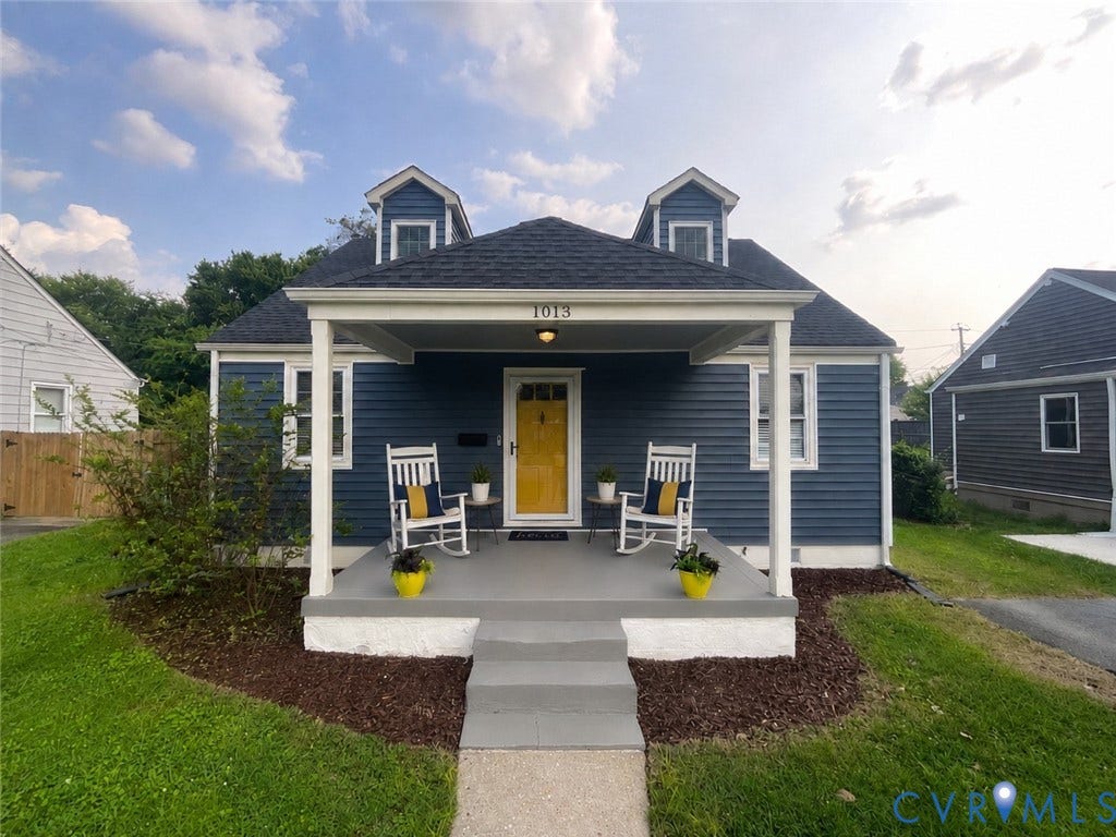 Front exterior with blue siding, a covered porch, white columns, a yellow front door, and two dormer windows