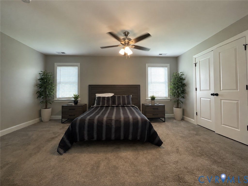Neutral tone wall color, plush carpet, two windows with blinds, ceiling fan with integrated lighting, and white bi-fold closet doors