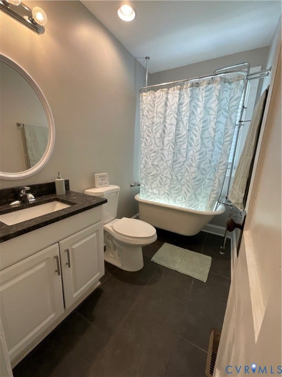 Dark-toned tile flooring, white vanity with dark countertop, classic clawfoot tub, recessed ceiling lighting, and wall-mounted vanity lighting fixture