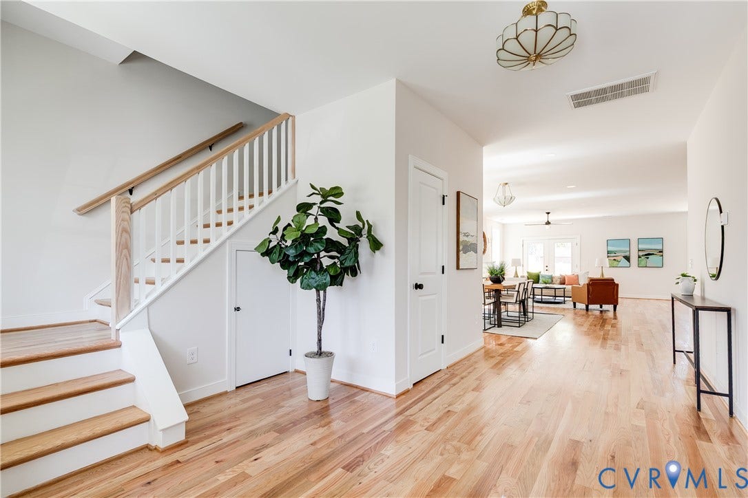 404 W 31st Street, Woodland Heights, Richmond, VA 23225 Light wood-finish flooring, staircase with wood handrails and white balusters, recessed storage beneath the staircase, and an open layout to a living area with a ceiling fan
