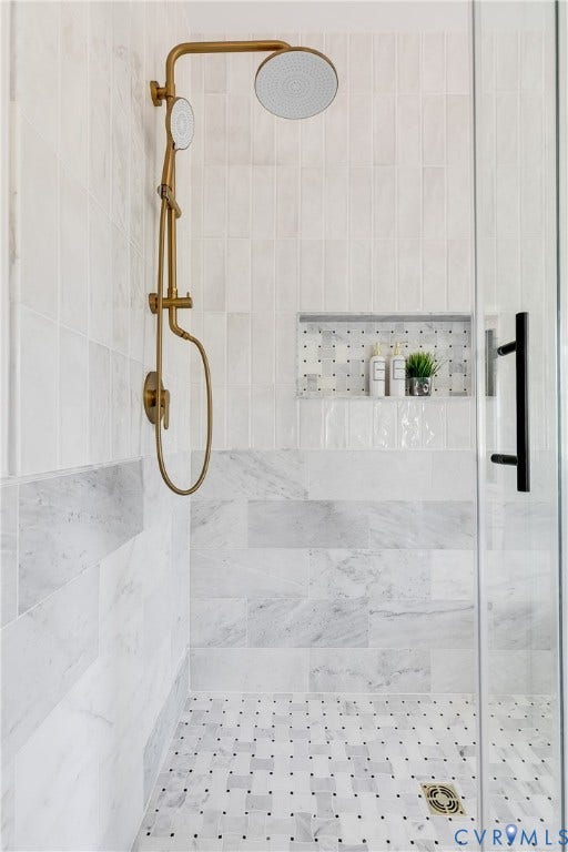 404 W 31st Street, Woodland Heights, Richmond, VA 23225 Shower enclosure featuring a frameless glass panel, brass-finish shower fixtures, a tiled shower niche, and variegated white and gray wall tiling