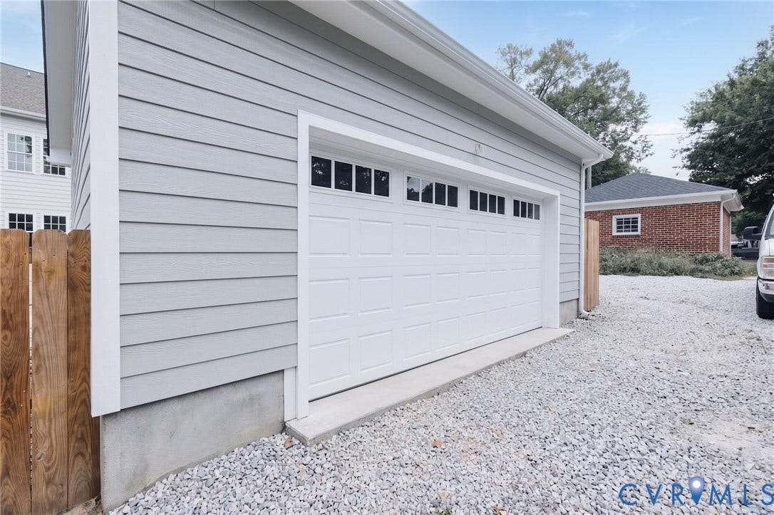 404 W 31st Street, Woodland Heights, Richmond, VA 23225 Detached structure featuring light gray horizontal siding, white trim, a sectional garage door with upper window panels, and a gravel surface