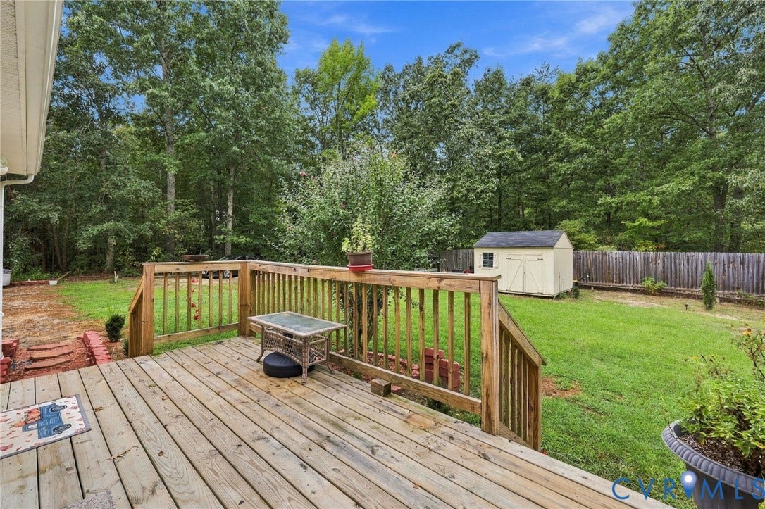 133 Ford Road, Bumpass, VA 23024 Wood-finish deck with railing, expansive green lawn, mature trees, and a detached storage shed