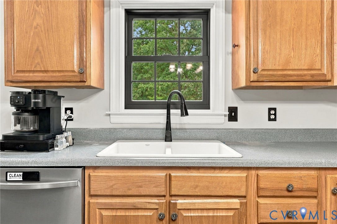133 Ford Road, Bumpass, VA 23024 Kitchen featuring warm wood cabinetry with recessed panel doors, gray quartz countertops, an undermount sink with matte black pull-down faucet, stainless steel dishwasher, and a multi-pane window framed by white trim overlooking landscaped grounds