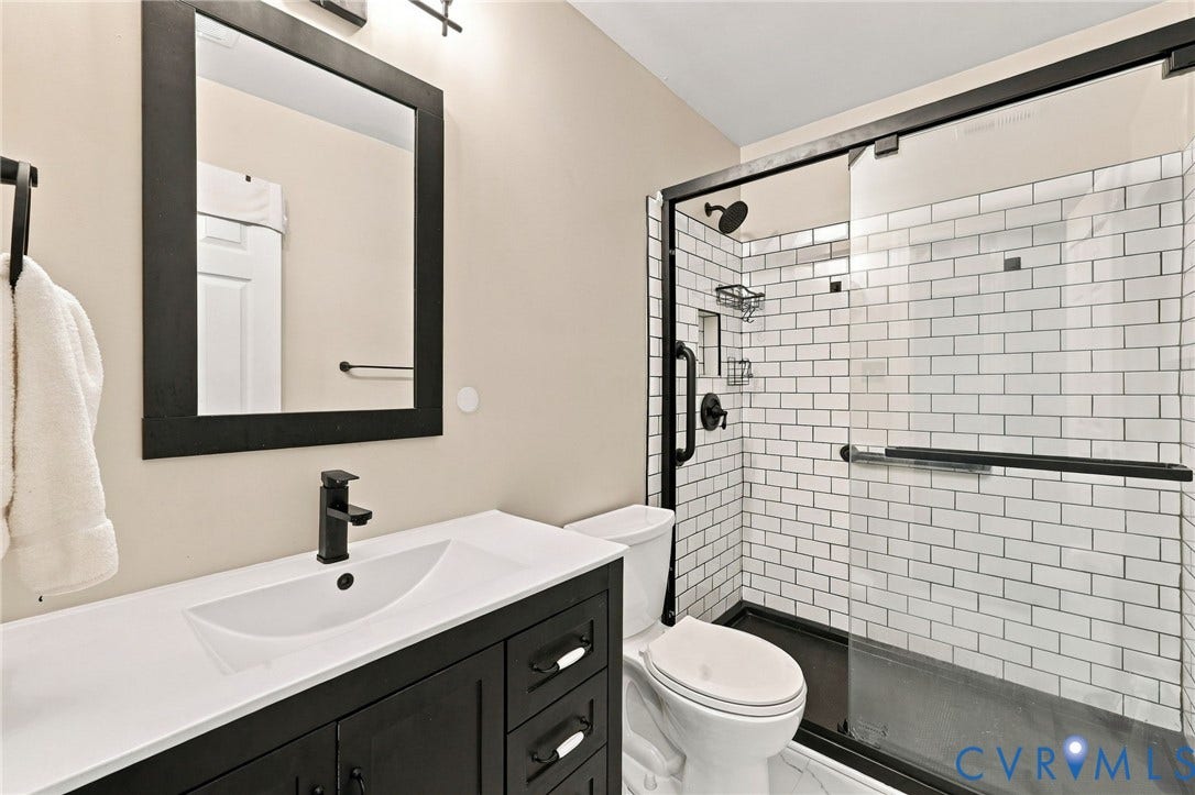 133 Ford Road, Bumpass, VA 23024 Bathroom featuring a vanity with an integrated sink and black cabinetry, a framed mirror, a walk-in shower with subway tile, and a glass shower enclosure
