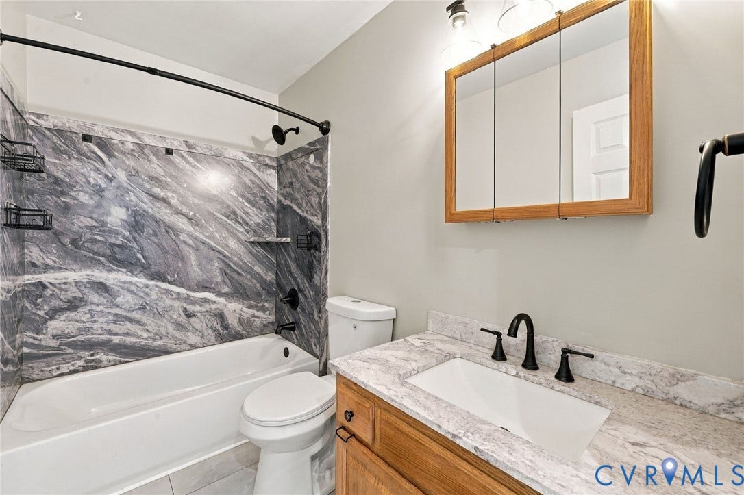 133 Ford Road, Bumpass, VA 23024 Bathroom featuring a bathtub with a marble-patterned surround, a single vanity with a countertop, a rectangular undermount sink, and matte black fixtures