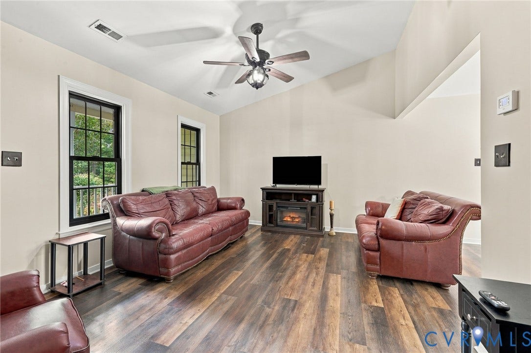 133 Ford Road, Bumpass, VA 23024 Vaulted ceiling with a ceiling fan, wood-finish flooring, recessed media console with an electric fireplace, and two windows with black framing