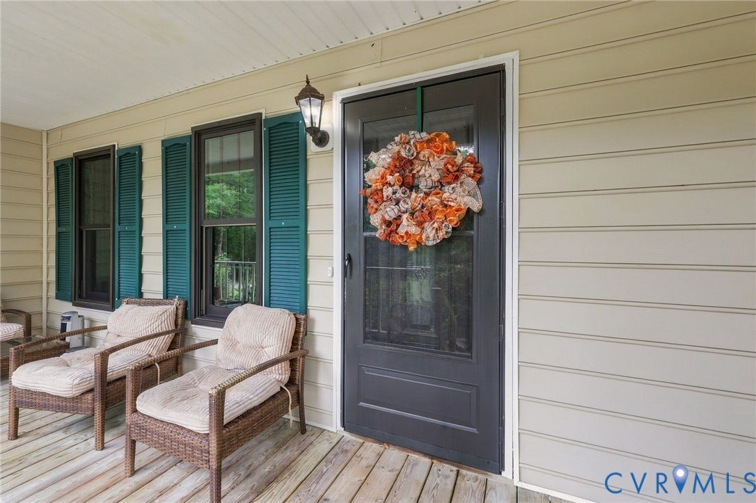 133 Ford Road, Bumpass, VA 23024 Covered porch with wood-finish decking, horizontal siding, black front door, and exterior wall lantern