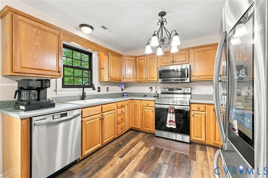 133 Ford Road, Bumpass, VA 23024 Wood-finish flooring, light wood cabinetry, white sink, stainless steel appliances, and a black-framed window