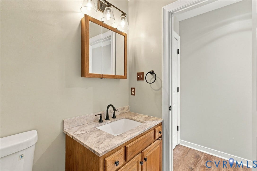 133 Ford Road, Bumpass, VA 23024 Wood-finish vanity with a light-toned countertop, undermount sink, and dark-finish faucet